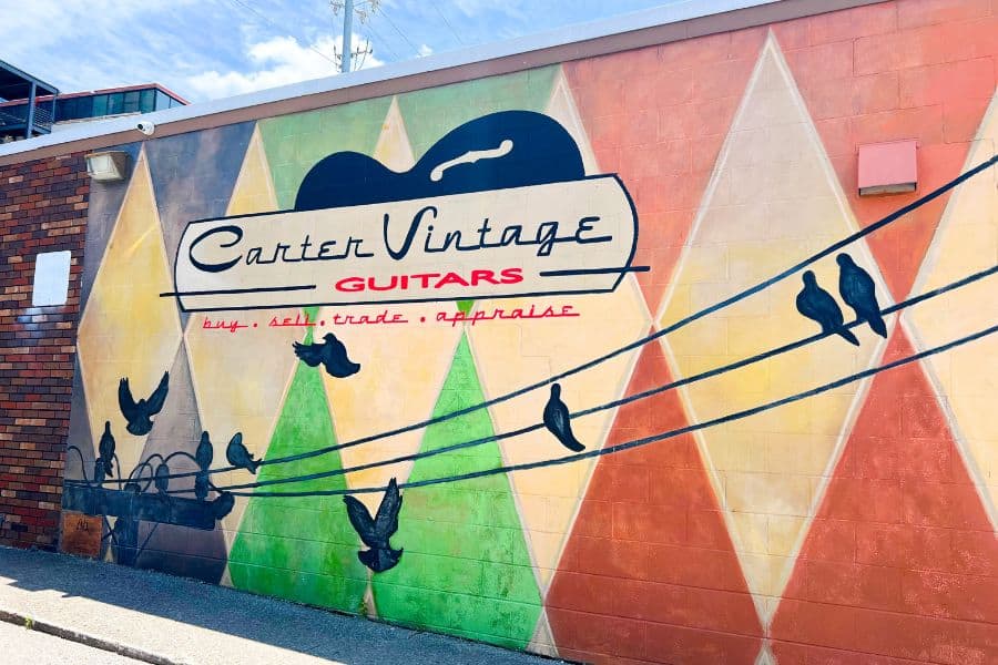 carter vintage guitars mural on the outside of the guitar shop. There are multiple colors and a telephone wire with birds perched on it painted on the side of the building