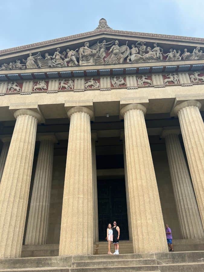 photo of of a couple standing in between the pillars of the replica Parthenon in Centennial Park in Nashville TN