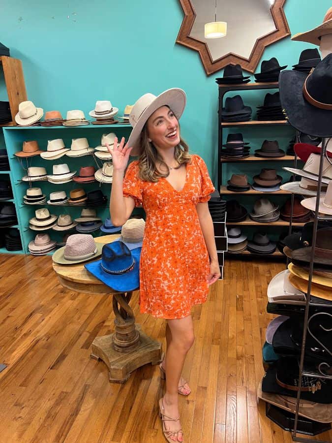 photo of a girl in an orange dress posing with a white wide brimmed hat in a hat shop