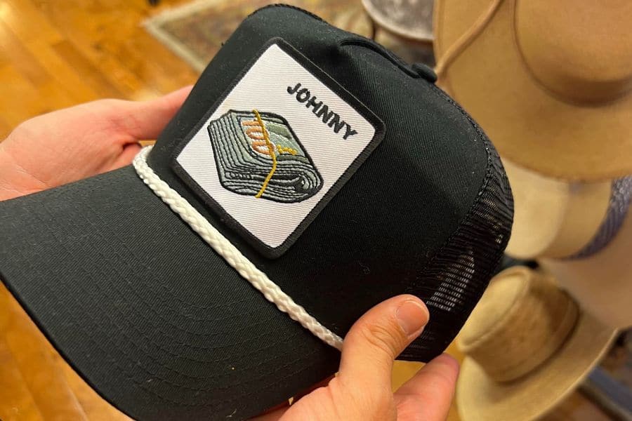 photo of a ball cap with the word "Johnny" embroidered on it and a stack of dollar bills below it. (Johnny Cash reference)