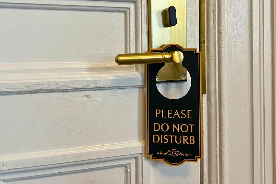 A Hotel door with a gold handle with a sign on the handle that says "Please Do Not Disturb"
