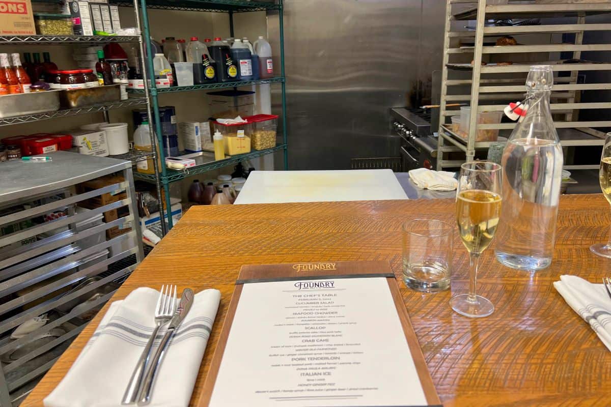 Chefs Table Dinner Experience at Foundry Table and Tap in Pittsburgh. Table set up in a kitchen area with a menu, glass of champagne, and and silverware