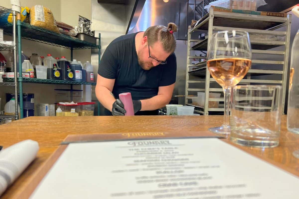 Chefs Table at Foundry Table and Tap in Pittsburgh PA. Chef is preparing food in front of a table setting with a glass of wine and and a menu