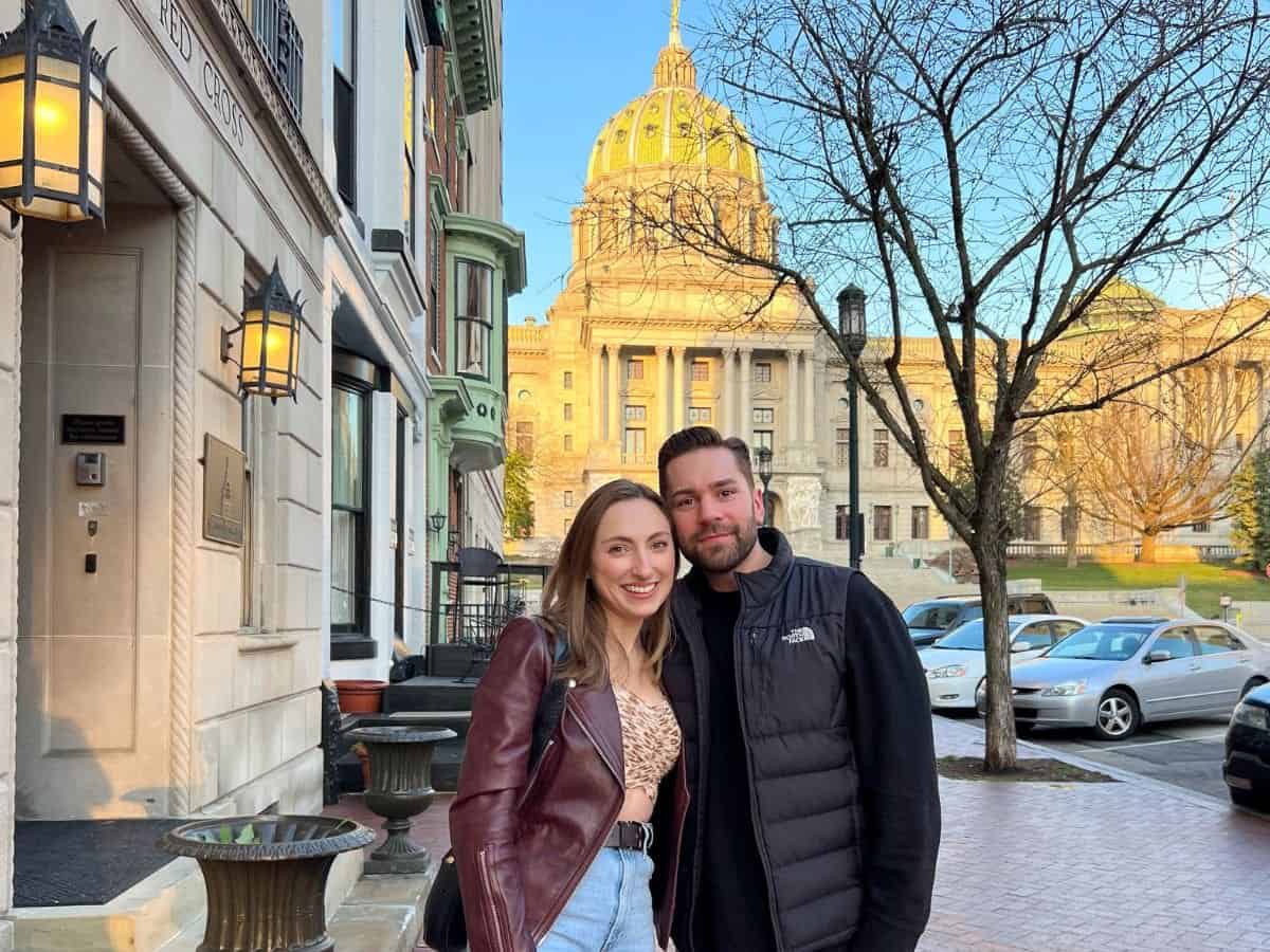 a young couple smiling on the street in downtown Harrisburg with the Pennsylvania capital building behind them